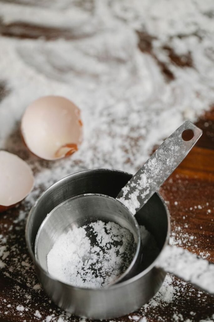 From above of stainless saucepans with eggshells on table with flour during cooking process