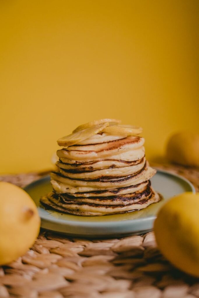 A stack of homemade pancakes garnished with lemons on a vibrant yellow background, perfect for breakfast themes.