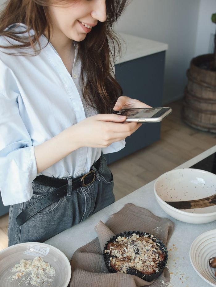 A woman uses her smartphone to capture a freshly baked berry pie in her kitchen.