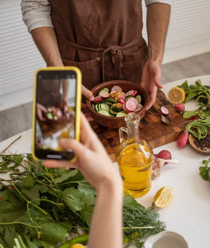 A person photographs a colorful vegetable salad bowl with a smartphone in a kitchen setting.